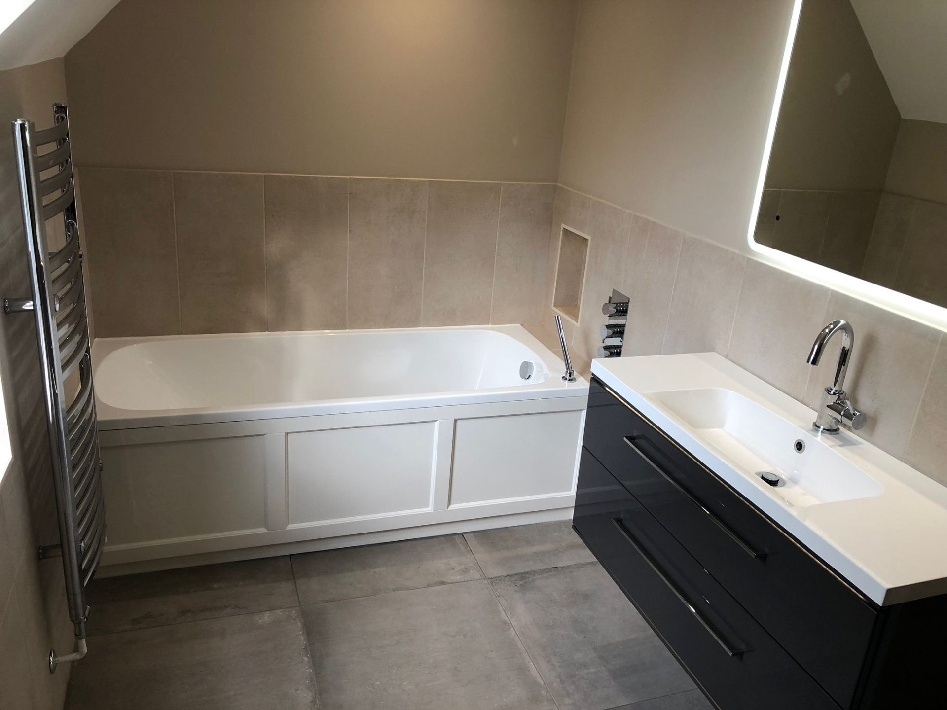 Fitted loft bathroom with panelled bath, chrome heated towel rail and back-lit LED mirror