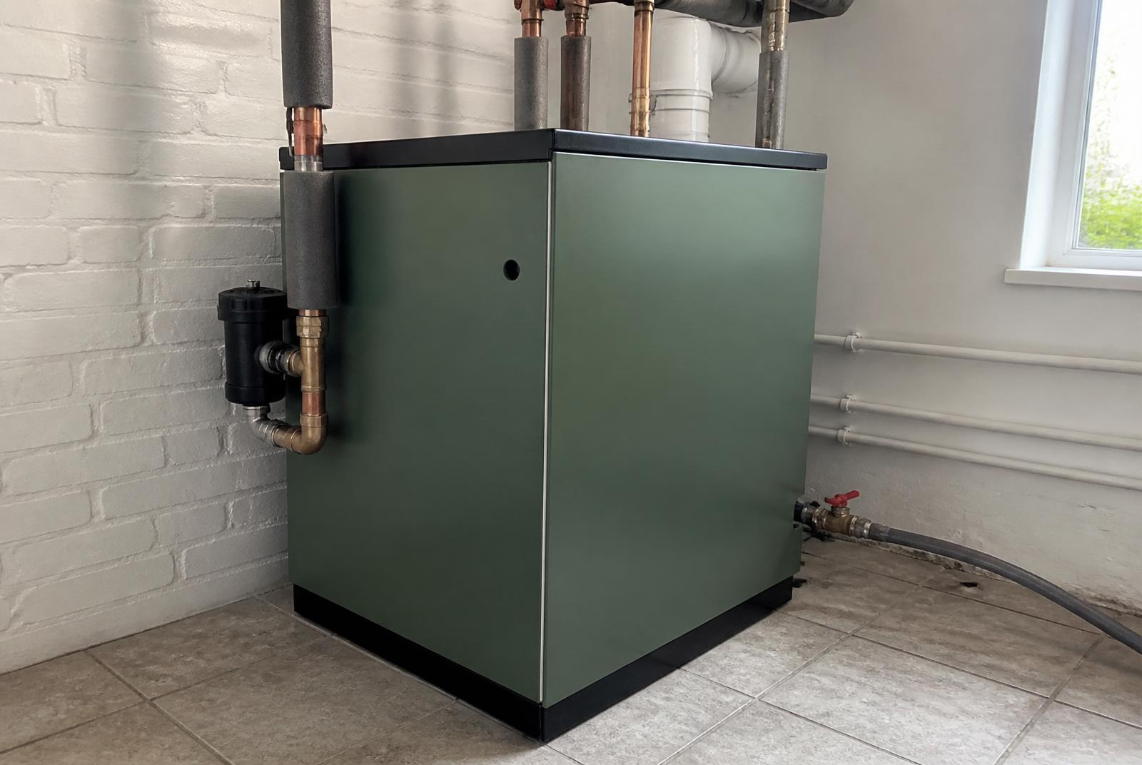 Green floor-standing oil boiler installed in a utility room with insulated copper flow and return pipework, system filter and flue